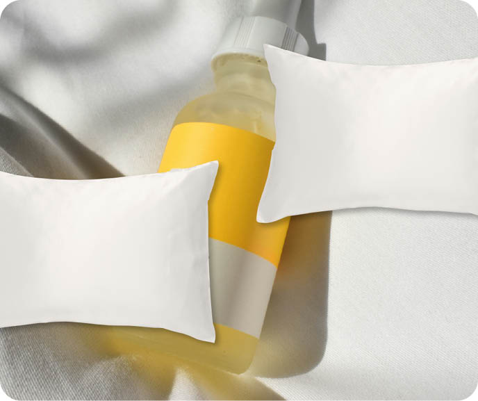 A small glass bottle containing skincare rests on a soft white background, with two of our 100% Mulberry Silk pillowcases in White overlaying the image. A small glass bottle containing skincare rests on a soft white background, with two of our 100% Mulberry Silk pillowcases in White overlaying the image.