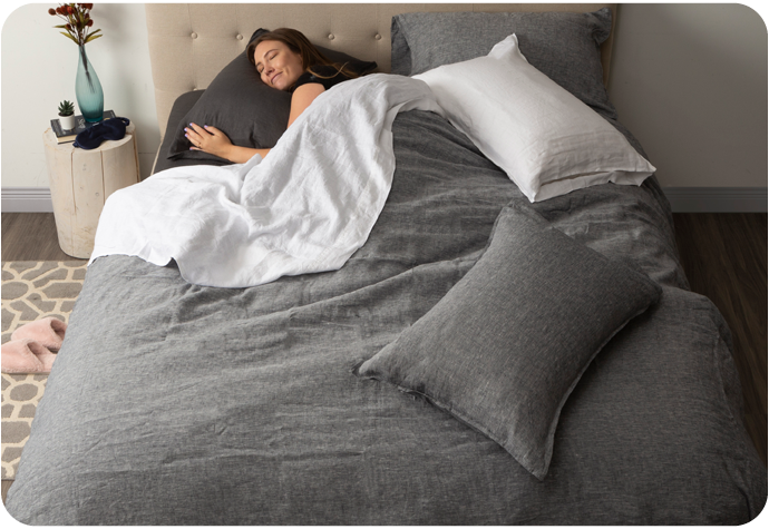Femme dormant dans un lit habillé de lin gris draps et d'une housse de couette en lin gris.