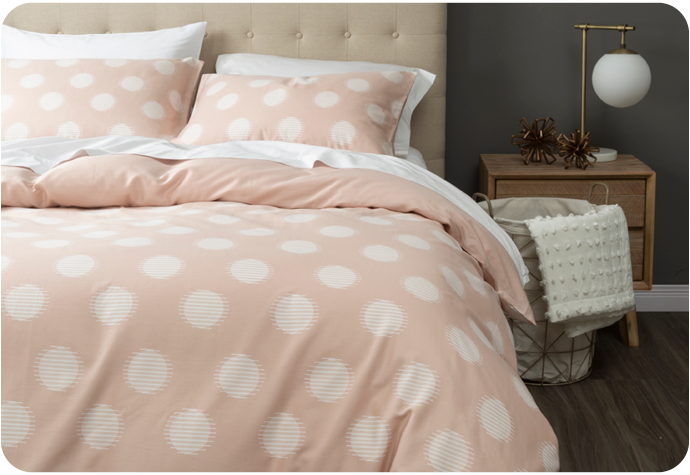 Vue de face de notre housse de couette en coton biologique rose à pois rose blush habillée sur un lit blanc dans une chambre grise.