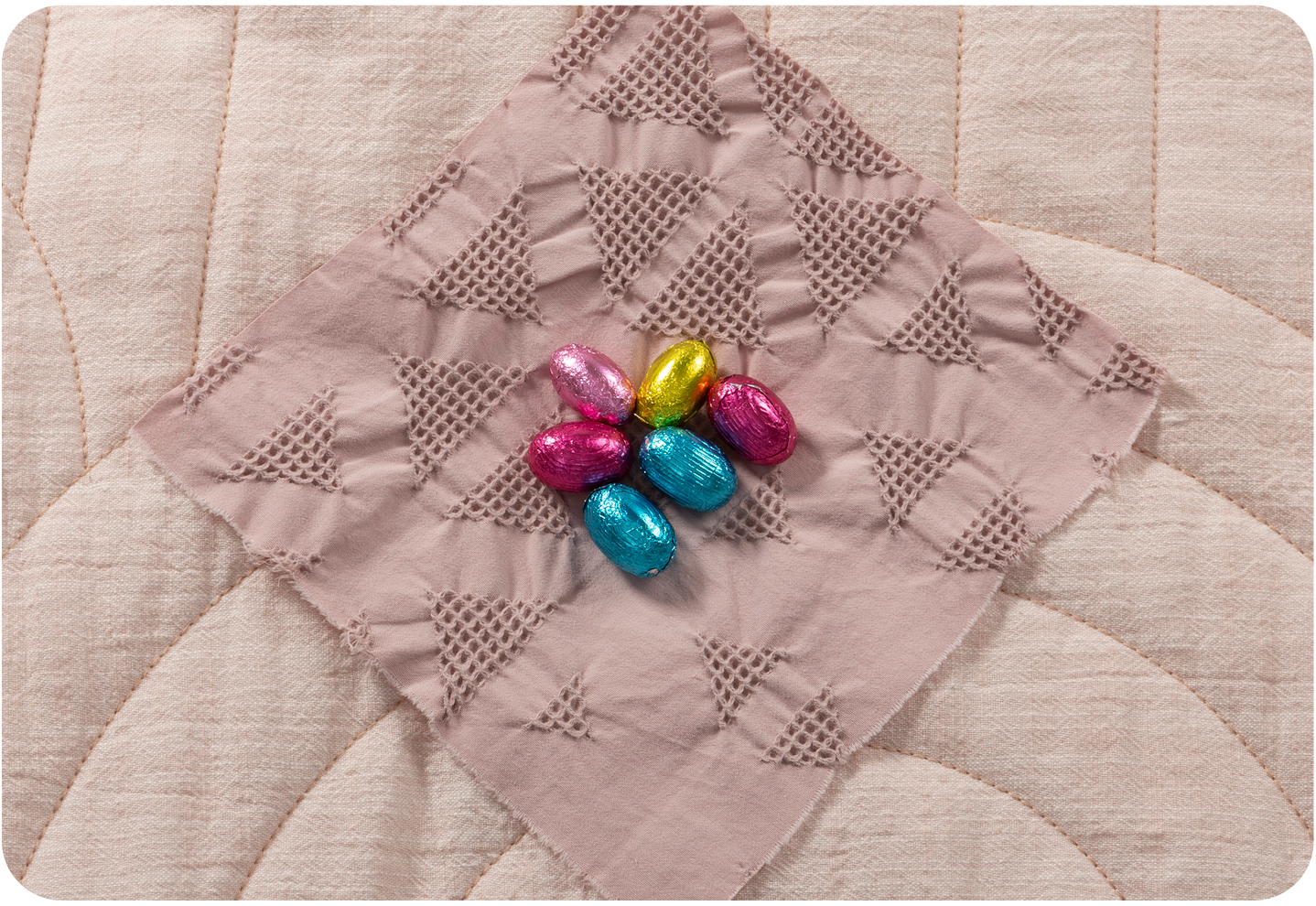 Des œufs en chocolat dans des emballages aux couleurs pastel vives au centre d'un losange de tissu.