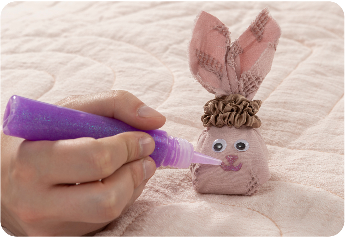 Dessiner à la main une bouche et un nez avec de la colle à paillettes violette sur la tête du lapin de Pâques DIY.