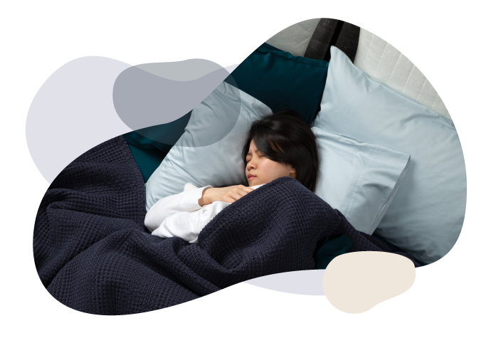 Femme dormant seule dans un grand lit bleu avec des oreillers sarcelle clair et une couverture bleu marine foncé.