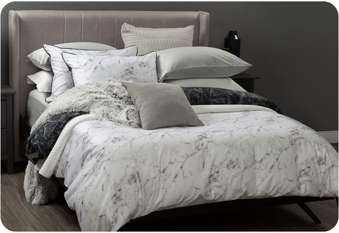 Notre housse de couette Bianco noire et blanche sur un grand lit avec plusieurs oreillers et coussins gris et blancs assortis par-dessus.