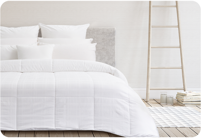 A white duvet with large box stitching sitting over a white bed in a blank bedroom, with a wooden ladder nearby.