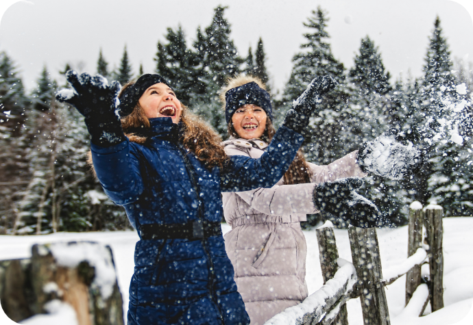 Two girls playing in the snow outside near a forest.