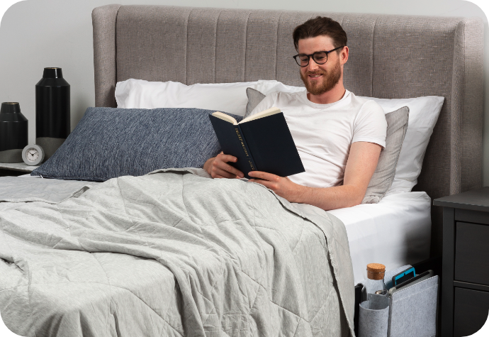 A young man reading in a bed dressed in grey and white tones.