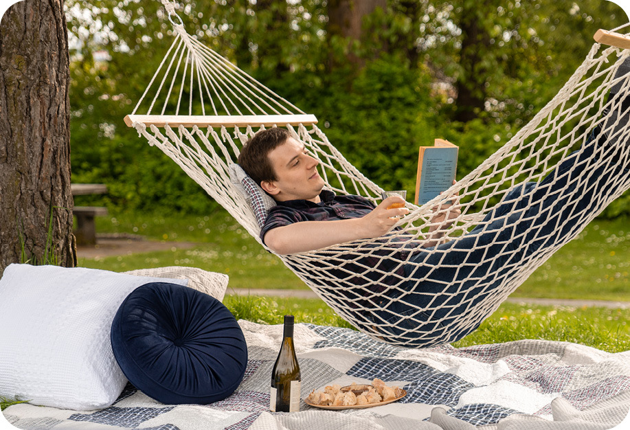Une personne se prélassant dans un hamac en lisant un livre, entourée de literie et d'accessoires QE Home.