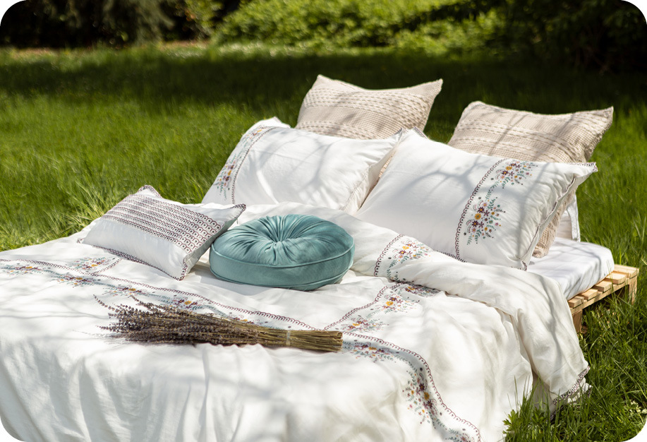 Un lit improvisé dans un pré herbeux, habillé de la collection Kaysa et de notre coussin rond en velours côtelé en aqua.