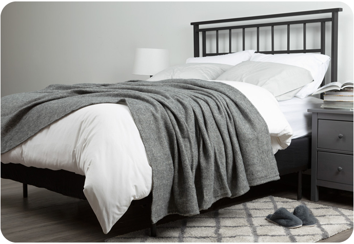 Notre couverture grise en laine Lismore présentée drapée sur un lit fait.