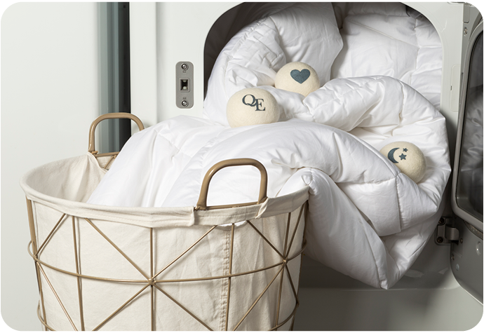Our Linen Love Wool Dryer Balls are shown on our duvet spilling out of a household dryer and into a laundry basket.