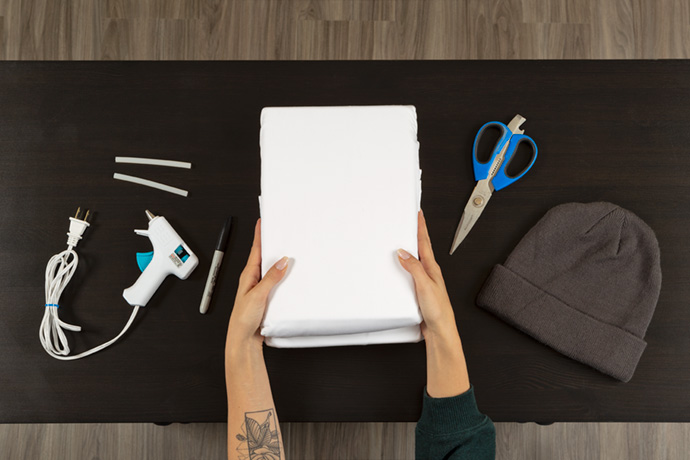 Top view of a glue gun, scissors, white sheet, and toque over a black table. Top view of a glue gun, scissors, white sheet, and toque over a black table.