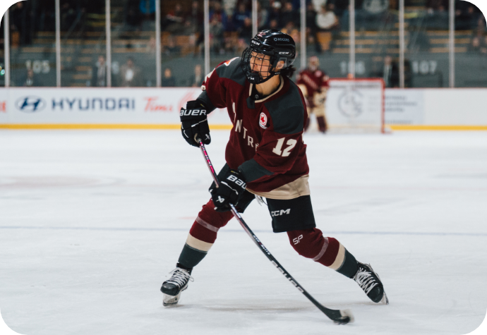 Hockey player Leah Lum in the official PWHL Montreal maroon and beige attire skating on the ice, poised to take a shot. 