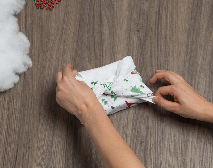 Deux mains attachant ensemble le haut d'un petit torchon en tissu pour emballage cadeau.