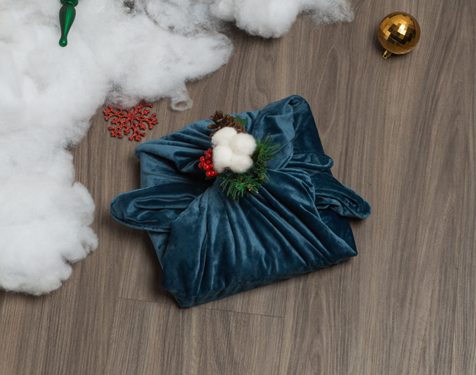 Folded blue square cushion cover used as fabric gift wrap with a mistletoe in the top knot.
