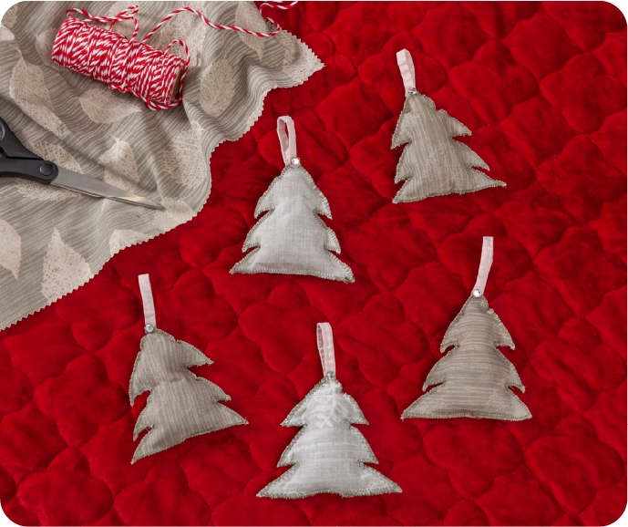 Our DIY Fabric Scrap Holiday Decorations shown on a red textile surface with scissors, fabric and string.