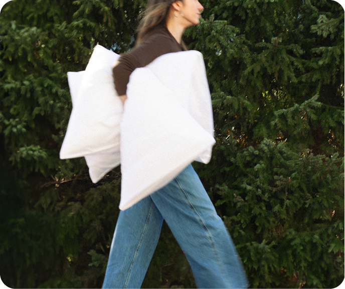 A person carrying two pillows walking in a forest.